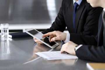 Businessman using tablet computer and work together with his colleague or partner at the glass desk in modern office, close-up. Unknown business people at meeting. Teamwork and partnership concept