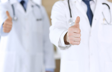 Group of modern doctors standing as a team with thumbs up or Ok sign in hospital office, close-up. Physicians ready to examine and help patients. Medical help, insurance in health care, best treatment