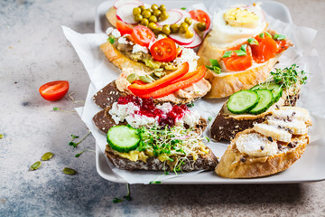 Open toasts with different toppings on gray-brown background. Crostini with banana, pate, avocado, salmon, egg, cheese and berries.