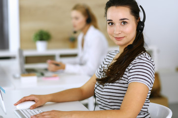 Business woman using headset for communication and consulting people at customer service office. Call center. Group of operators at work at the background. Casual dress style