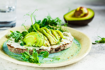 Rye bread toast with cream cheese and avocado on beautiful plate. Healthy breakfast concept.