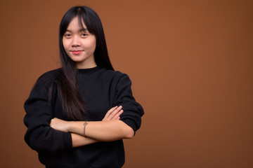 Young beautiful Asian woman wearing black sweater against brown