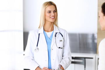 Doctor woman at work in hospital excited and happy of consulting female patient. Blonde physician controls medication history records and exam results while using clipboard. Medicine and healthcare