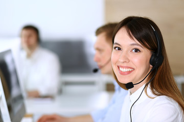 Call center. Group of diverse operators at work. Focus on beautiful asian woman in headset at customer service office. Business concept