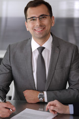 Businessman headshot at meeting in modern office. Entrepreneur sitting at the table with colleagues. Teamwork and partnership concept. Grey blazer suits to happy smiling manager