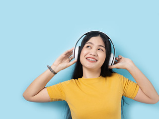 Happy Asian woman in yellow dress using headphone with pink background.