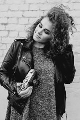 monochrome portrait of young beautiful woman with curly hair taking pictures on film oldfashioned camera on white bricks wall background. Film stylization