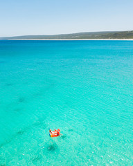 Fototapeta na wymiar Young woman floating away on a parrot inflatable in the stunning light blue water at Hamelin Bay, Western Australia.