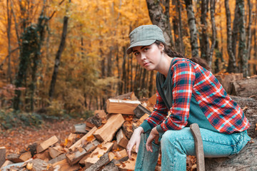 Preparation for the heating season. A pretty young woman sits on a log with an axe at her feet. In the background autumn forest. Close up