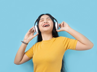 Happy Asian woman in yellow dress using headphone with blue background.