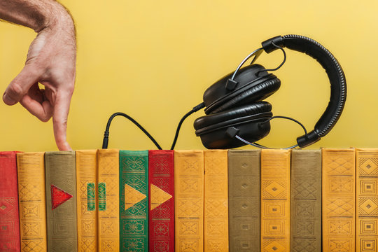 Education and modern technologies. The concept of audio books and media players. Vintage books are in a row, they are headphones. A man's hand presses the book with the PLAY icon. Yellow background