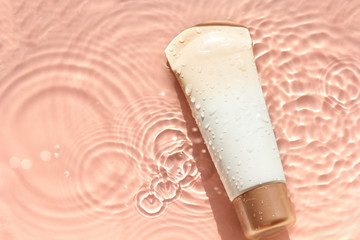 Sunscreen cream to remedy skin from sun on light water surface, top view. Concept ultraviolet protection, summer cosmetics.