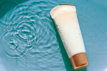 Sunscreen cream to remedy skin from sun on blue water surface of pool, top view. Concept ultraviolet protection, summer cosmetics.