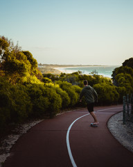 Lone skater, skating through the beach shrubs down the path at Mullaloo beach lookout towards the...