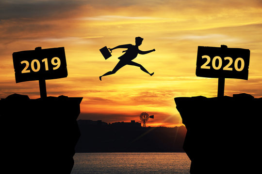 Businessman jumping between 2019 and 2020 years with sunset background