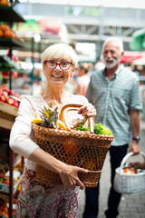 Smiling senior couple holding basket with vegetables at the market