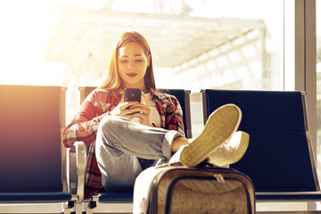 Air travel concept with young casual girl sitting with hand luggage suitcase. Airport asian woman...