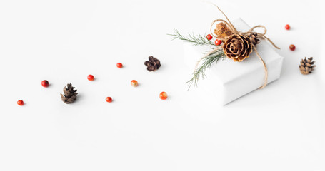 Christmas composition of natural materials. Christmas gift wrapped in craft paper, knitted blanket, pine cones, fir branches on white background. Flat lay, top view, with copy space.