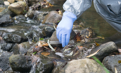 hand in blue in a protective glove, pours liquid from a test tube into a riverbed