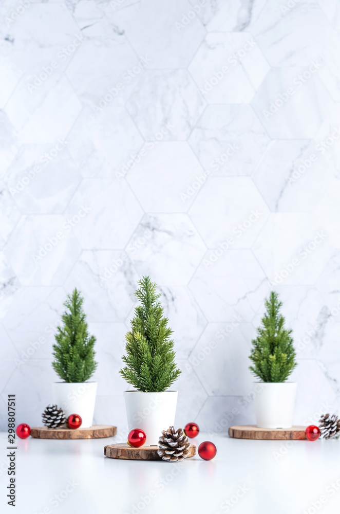 Poster Three christmas tree with pine cone and decor xmas ball on white table and marble tile wall background.clean minimal simple style.holiday still life mockup banner with space to adding text