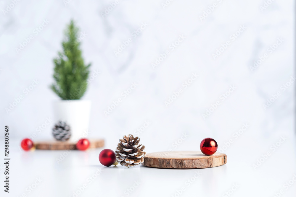 Poster christmas tree with pine cone and decor xmas ball and empty wood log plate on white table and marble tile wall background.clean minimal simple style.holiday still life mockup to display design