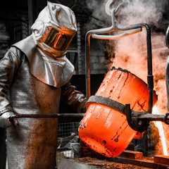 In a foundry workshop. A worker protected by a safety suit pours the molten metal into a mold