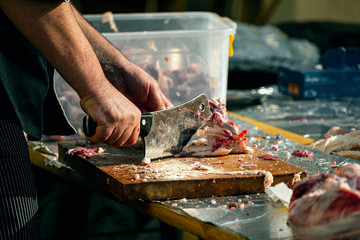 The butcher cuts a piece of meat with sharp cleaver knife at food festival