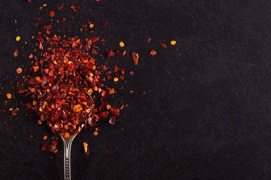 Crushed dried chili peppers in an iron spoon scattered on a black background. Concept, copy space.