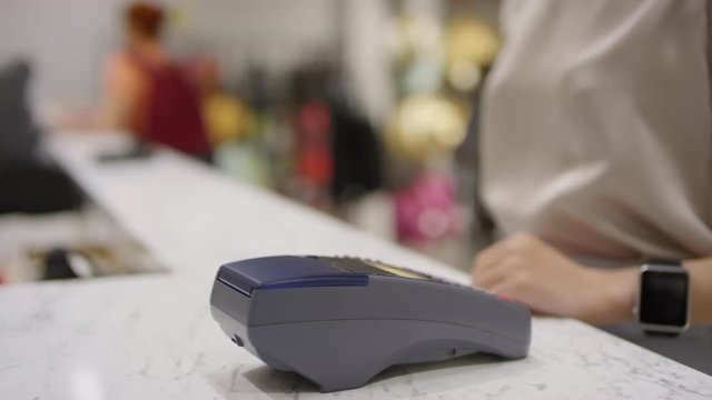 Lockdown arc shot of payment terminal on checkout counter at store, unrecognizable woman pressing smart watch to it, taking shopping bags and walking away