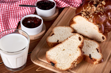Still life with knitted Christmas cake or sweet pastry with raisins and almonds. Slices on old wooden mat with bowls with fruit jam and glass of milk