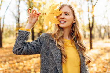 Happy young girl smiling with autumn yellow leaf in Park
