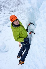 Fototapeta na wymiar Alpinist man with ice tools axe in orange helmet climbing a large wall of ice. Outdoor Sports Portrait.