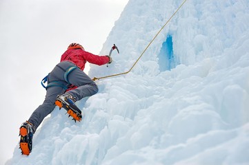 Alpinist woman with ice tools axe in orange helmet climbing a large wall of ice. Outdoor Sports...