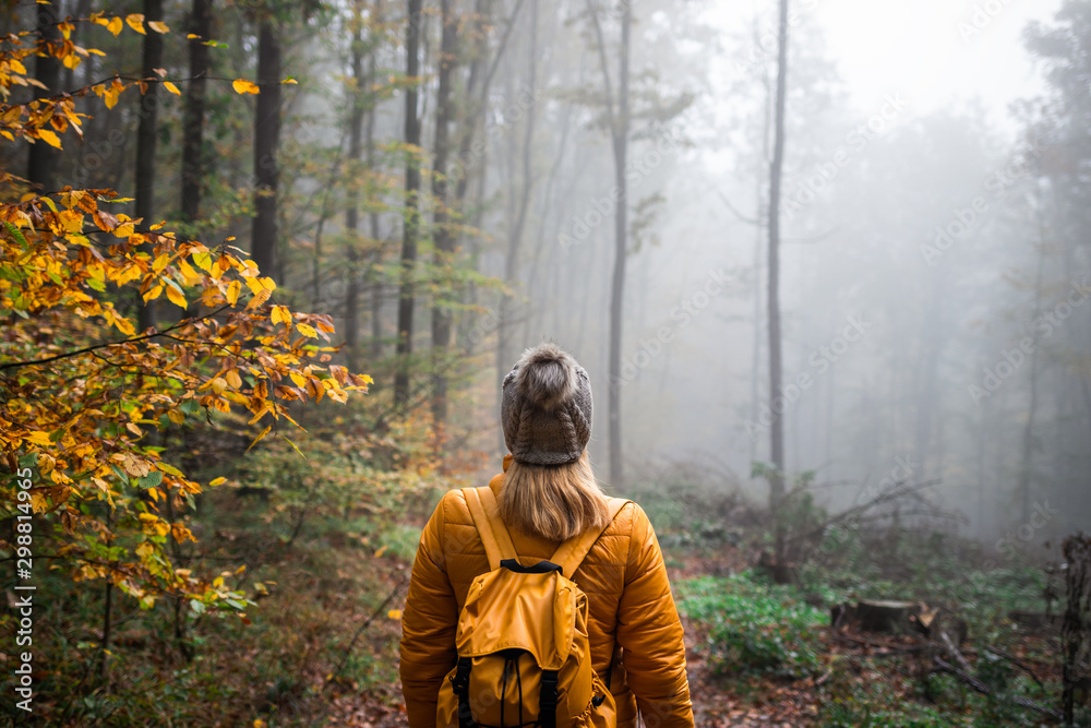 Wall mural woman with knit hat and backpack hiking in foggy woodland