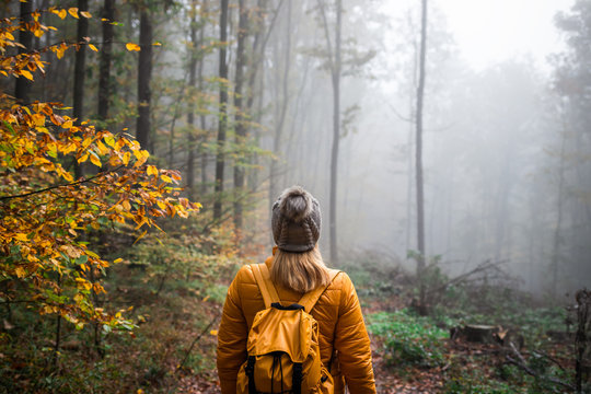 Woman with knit hat and backpack hiking in foggy woodland