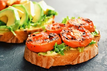 Bruschetta on a dark table background. Bruschetta with grilled  tomatoes, mozzarella and avocado. Delicious vegetarian healthy sandwiches. Tasty snack.