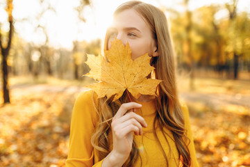 Happy young girl smiling with autumn yellow leaf in Park