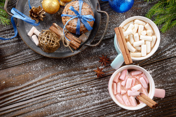 Flat lay Christmas background of two mugs of hot chocolate with marshmallows, spruce branch and tray with gingerbread cookies on wooden table