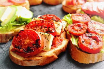 Bruschetta on a dark table background. Bruschetta with tomatoes, mozzarella and avocado. Delicious vegetarian healthy sandwiches. Tasty snack on the pink plate.