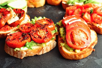 Bruschetta on a dark table background. Bruschetta with tomatoes, mozzarella and avocado. Delicious vegetarian healthy sandwiches. Tasty snack on the pink plate.