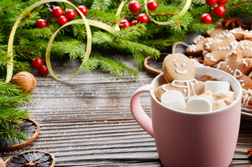 Pink mug with hot chocolate marshmallows and gingerbread man on background of spruce branch and...