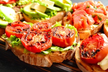 Bruschetta on a dark table background. Bruschetta with grilled  tomatoes, mozzarella and avocado. Delicious vegetarian healthy sandwiches. Tasty snack.