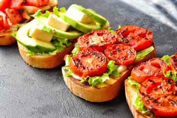 Bruschetta on a dark table background. Bruschetta with grilled  tomatoes, mozzarella and avocado. Delicious vegetarian healthy sandwiches. Tasty snack.