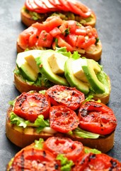 Bruschetta on a dark table background. Bruschetta with grilled  tomatoes, mozzarella and avocado. Delicious vegetarian healthy sandwiches. Tasty snack.