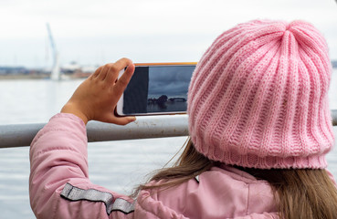 a little girl takes photos with her phone of the sea