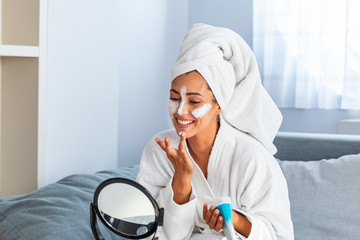 Spa at home. Woman at home is applying facial sheet mask. Cosmetic procedures, mask for skin care,...