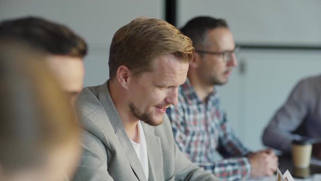 Tracking shot of two middle aged men whispering in meeting sharing secrets. Group of business people sitting on desk