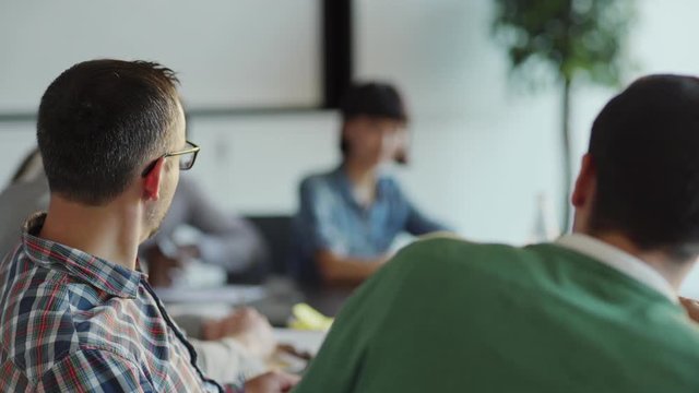 Tracking shot of two middle aged men having discussion while sitting at desk during business meeting with colleagues