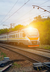 Naklejka premium commuter train rides on railway tracks in city with green trees in background