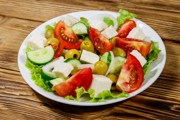 Greek salad with fresh vegetables, feta cheese and green olives on wooden table